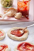 Mini-Pizzafladen mit Tomatenpüree bestreichen