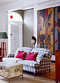 Living room with checked sofa, chest serving as coffee table & artworks on boards