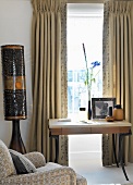 Small desk below window with traditional curtains and Africa-style standard lamp