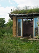 Offene Terrassentür eines organisch gestalteten Lehmhauses mit Gründach