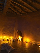 Burning fire in fireplace aperture and candlelight in clay house with simple roof structure
