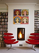Bücherzimmer mit Pop-Art-Bild über brennendem Kaminfeuer und modernen, roten Drehsesseln