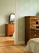 Antique chest of drawers with mirror and antique bureau in two rooms with floral wallpaper