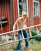 Woman with ladder in front of rust-red wooden house facade