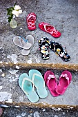 Assorted pairs flip flops on a mossy stone floor