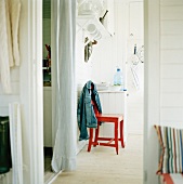 A red lacquered kitchen chair with a jacket hanging over the back next to a hallway with a white curtain