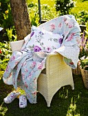 Wicker chair with a quilt and pillows in the garden