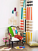 Various swatches of fabric on antique chair with white upholstery next to curtain with multi-coloured stripes