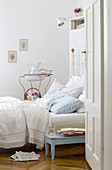 View through open bedroom door of comfortable country house bed and antique metal washstand with basin in background