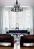 Schwarze Designer Sofas aus den 60er Jahren und schmiedeeiserner Kerzenleuchter vor Fenstererker in Altbau-Wohnzimmer