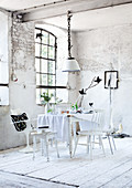 Dining table with tablecloth and white chairs in front of lattice window in dilapidated room in former factory