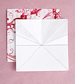 Series of photos showing steps for folding a paper flower from red and white patterned origami paper