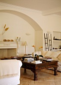 Antique coffee table and white sofas in front of open fireplace in arched surround