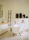 Vintage bathtub in centre of bathroom and group of black vases on shelf