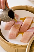 Marinade being poured over fish fillets in a bamboo steamer