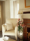 Elegant armchair with white cover and bouquet of lilies next to brick fireplace