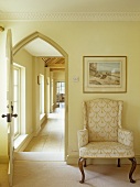 Sessel im Barockstil neben offener Tür mit spitzbogenförmigen Rahmen und Blick in Korridor