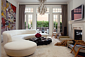 Elegantes Wohnzimmer mit überdimensionaler, weisser Couch, einem Couchtisch aus lackiertem Teakholz und weißem Flokatiboden; im Hintergrund die offene Terrassentür
