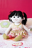 Hand-made rag doll with black wool pigtails against bright pink wall