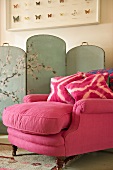 Antique armchair upholstered in pink velvet with cushions in front of painted screen with Chinese motif