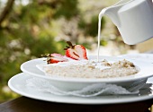 Milk Pouring from a Pitcher onto a Bowl of Oatmeal with Strawberries; Outdoors