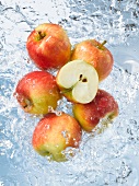 Red apples, whole & halved, dropping into water
