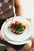 Woman serving plate of lamb fillet and vegetables