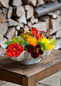 Colourful flower arrangement of nasturtiums, dill and French marigolds in old jelly mould on wooden table