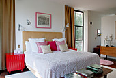 Scatter cushions arranged on double bed between two floor-to-ceiling windows with floor-length curtains in classic, modern bedroom