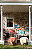 Seats with colourful cushions and animal furs on a covered terrace in front of a historic brick facade