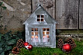 Festive garden decoration: little zinc cottage with candles on bed of moss