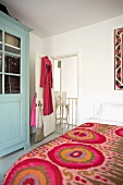 Feminine bedroom with a jazzy, colorful bedspread, dressing gown with red hearts and blue pastel country style cupboard