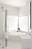 Elegant designer bathroom with corner bath tub in front of a window and closed blinds