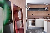 Blick in eine moderne Küche mit grauem Steinfliesenboden und einem Spritzschutz aus Holz