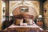 Pile of cushions on bed with antique wooden frame in front of Rococo wall panel in the shape of a portal