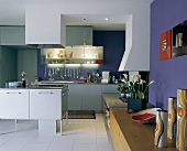 Designer kitchen island with extractor hood in front of kitchen counter in open-plan interior with sideboard against blue wall