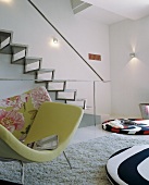 Sessel mit grünem Bezug vor moderner Metalltreppe an Wand und bunte Bodenpolster in Designer Wohnraum