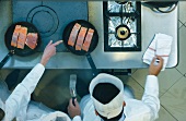 Chefs frying salmon fillets in a commercial kitchen