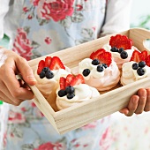 A person holding a wooden tray of meringue nests
