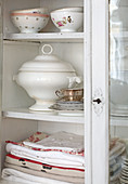 Table linen and crockery in glass-fronted cabinet with open door