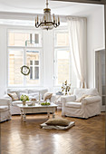 Sofagarnitur mit weissen Hussen und Couchtisch unter Kronleuchter im Wohnzimmer-Erker einer Altbauwohnung