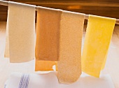Sheets of pasta hanging from a wooden spoon to dry