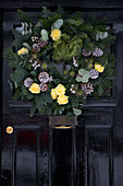 Christmas wreath with silver-painted pine cones and yellow roses on old front door