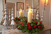 Lit candles in arrangement of roses and stylised metal fir trees in front of hall mirror