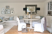 Weisses Wohnzimmer im romantisch eleganten Landhausstil mit Hussenstühlen an rundem Esstisch neben Durchreiche zur Küche