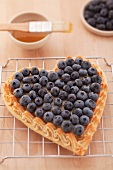 A heart-shaped blueberry tart on a wire rack