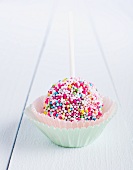 A cake pop decorated with sugar beads in a paper case