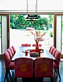 Upholstered chairs with patterned covers at dining table in front of open terrace door showing view of garden