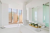 Puristisches Badezimmer mit Doppelwaschtisch und Badewanne vor drehbaren Rattanelementen als Sichtschutz
