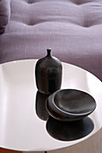 Black-glazed ceramic vessels on reflective metal top of side table; detail of sofa in background